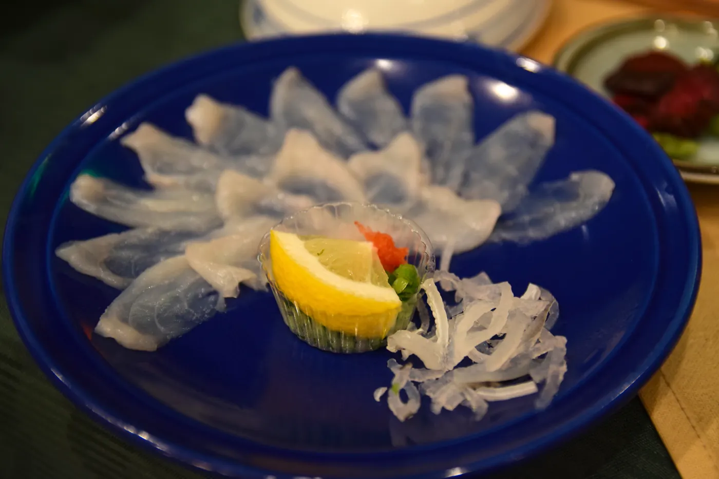 Photograph of thinly sliced fugu sashimi served on a deep blue dish